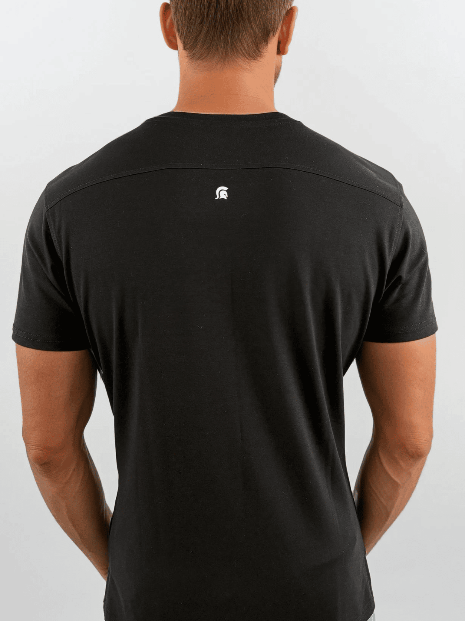 Person wearing a black t-shirt with a logo on the back against a light gray background