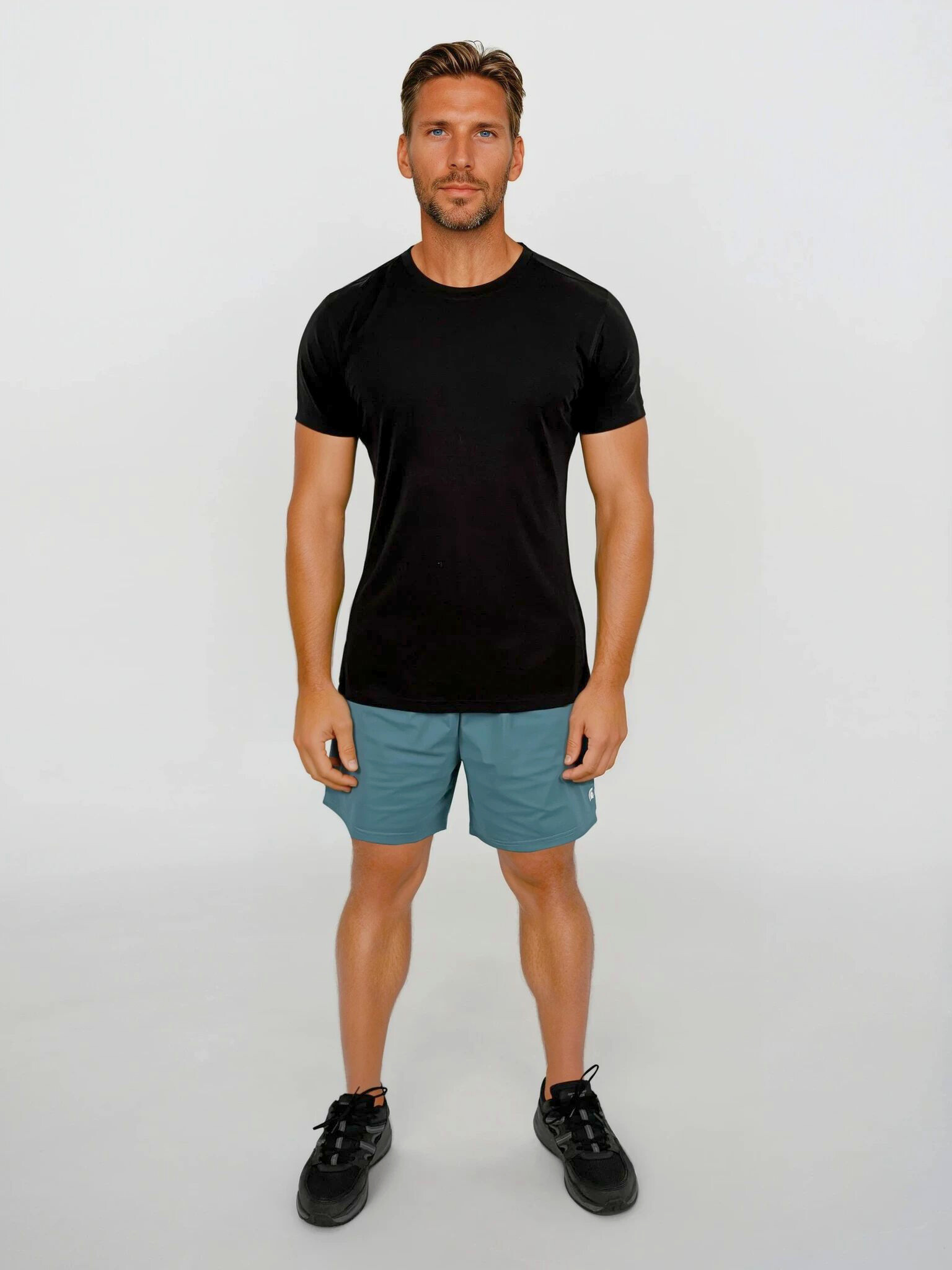 Man wearing a black t-shirt and teal shorts on a white background