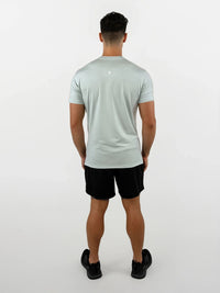 Man wearing a light green t-shirt and black shorts on a white background