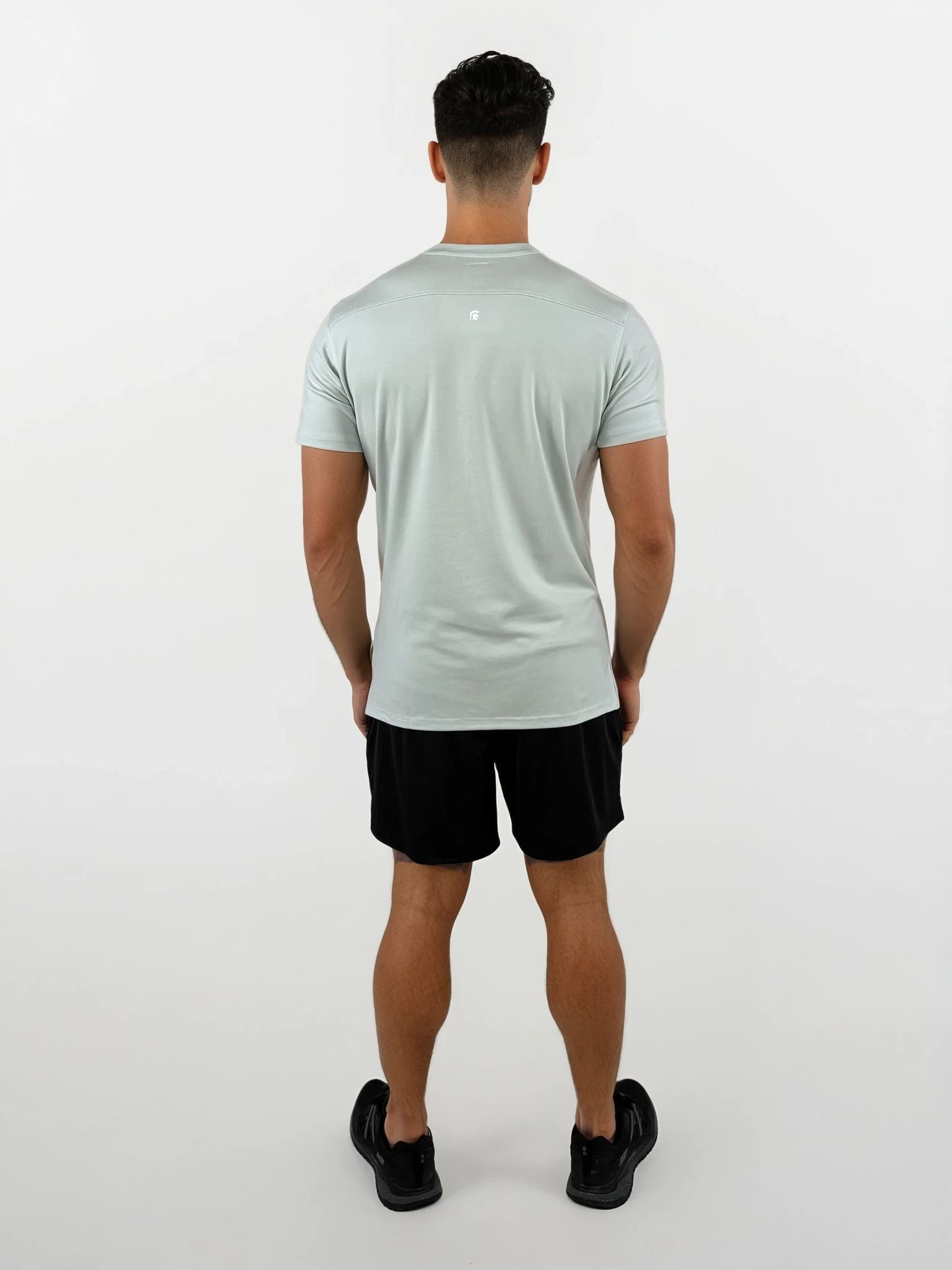 Man wearing a light green t-shirt and black shorts on a white background
