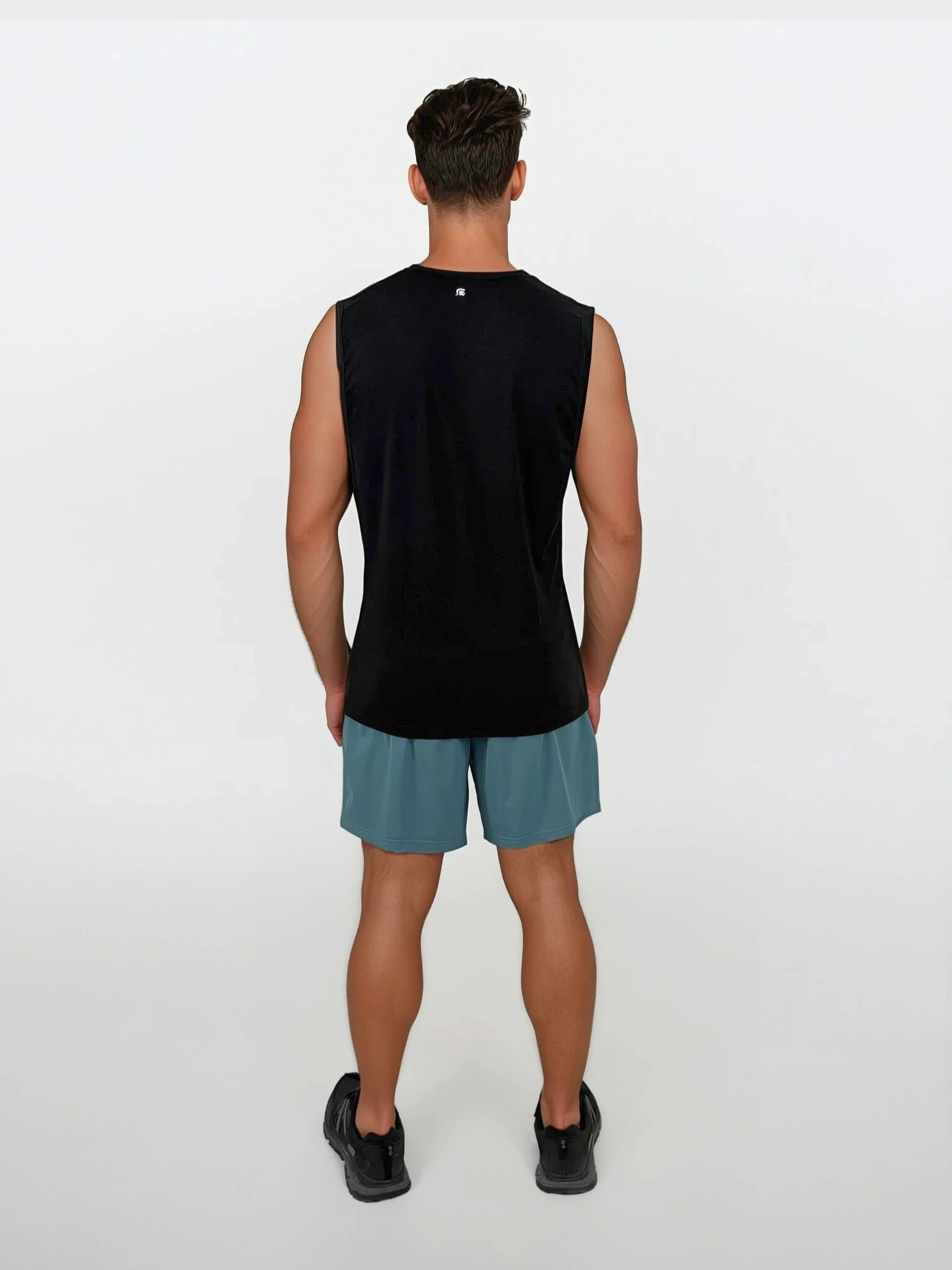 Person wearing a black sleeveless shirt and teal shorts on a white background
