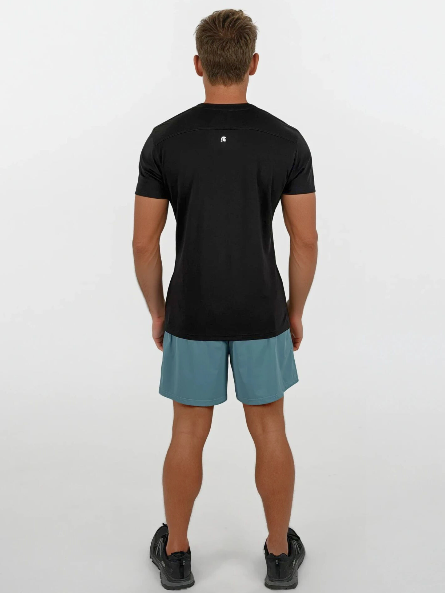 Man wearing a black t-shirt and teal shorts on a white background
