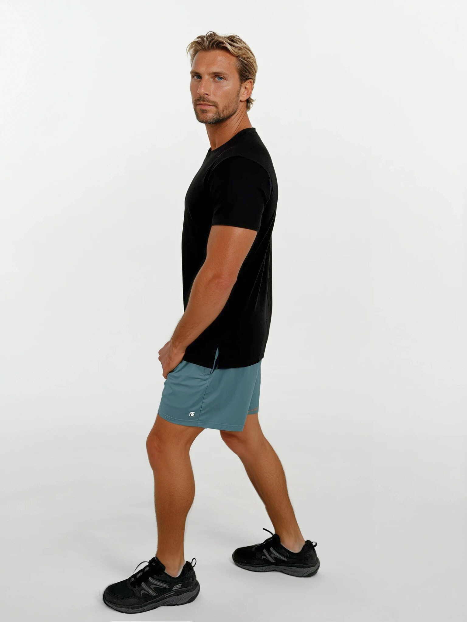 Man wearing a black t-shirt and teal shorts on a white background