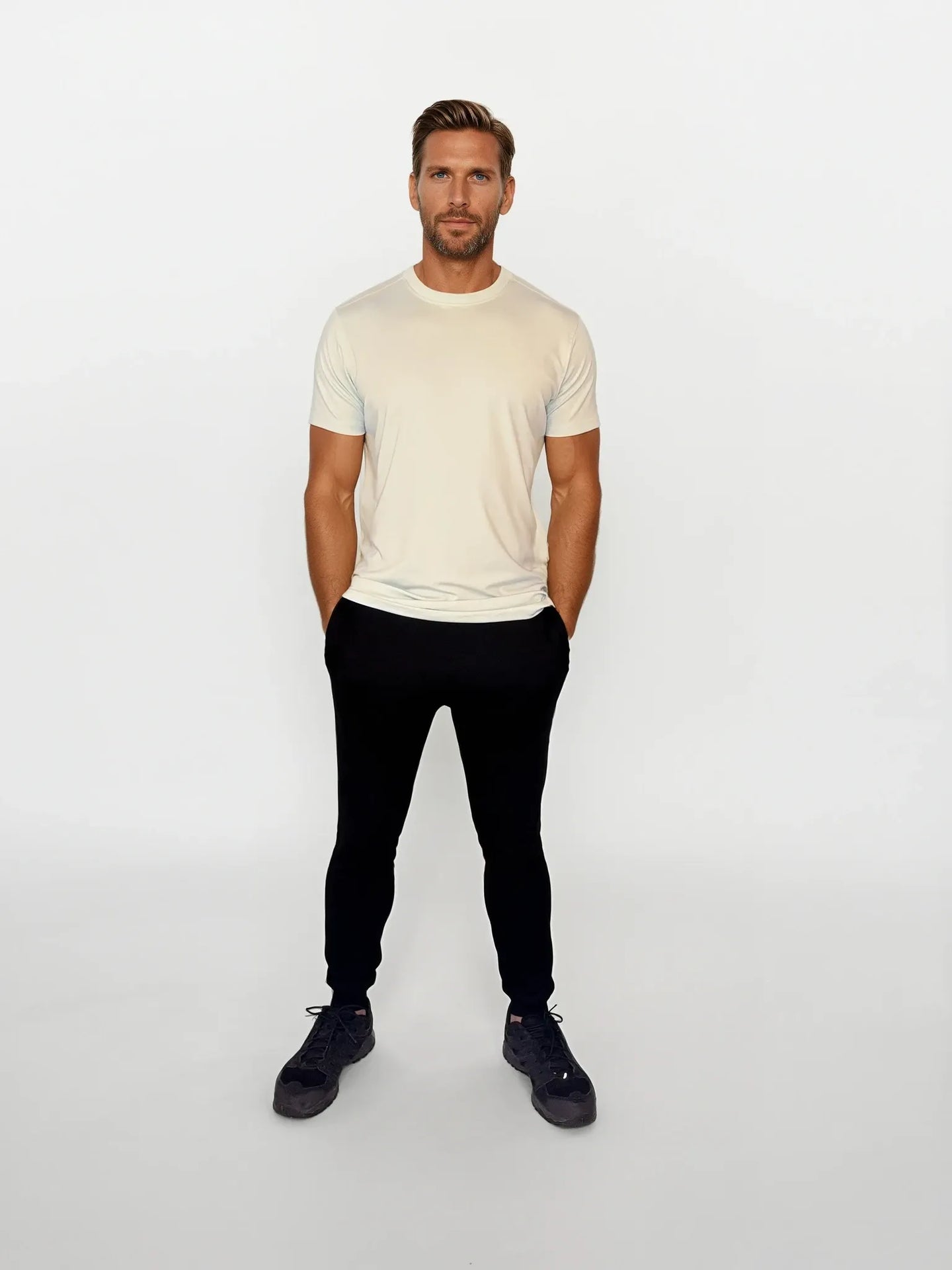 Man wearing a cream t-shirt and black pants on a white background