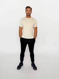 Man wearing a cream t-shirt and black pants on a white background