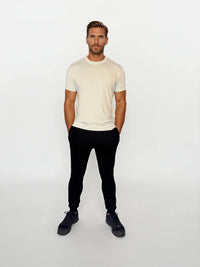 Man wearing a cream t-shirt and black pants on a white background
