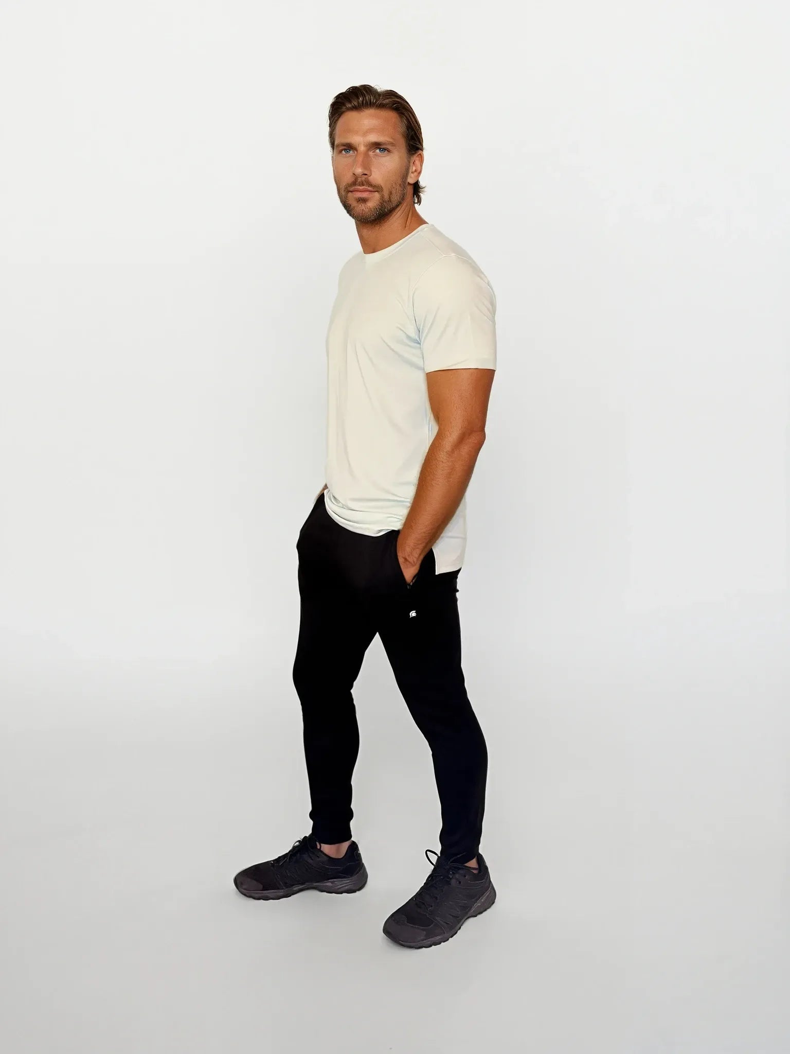 Man wearing a white t-shirt and black pants on a light gray background