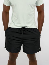 Person wearing black shorts and a light green t-shirt on a white background